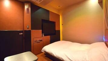 Una habitación de hotel con cama, una mesita, televisor montado en la pared y un armario.