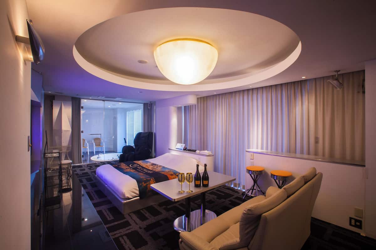 A hotel room with a bed, a seating area with a table, a sofa, and a large window with curtains.