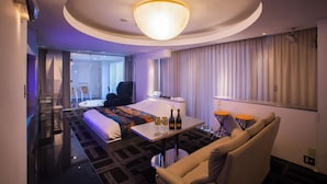 A hotel room with a bed, a seating area with a table, a sofa, and a large window with curtains.