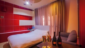 A hotel room with a bed, a table with two champagne glasses and a bottle, a sofa, and a curtain.