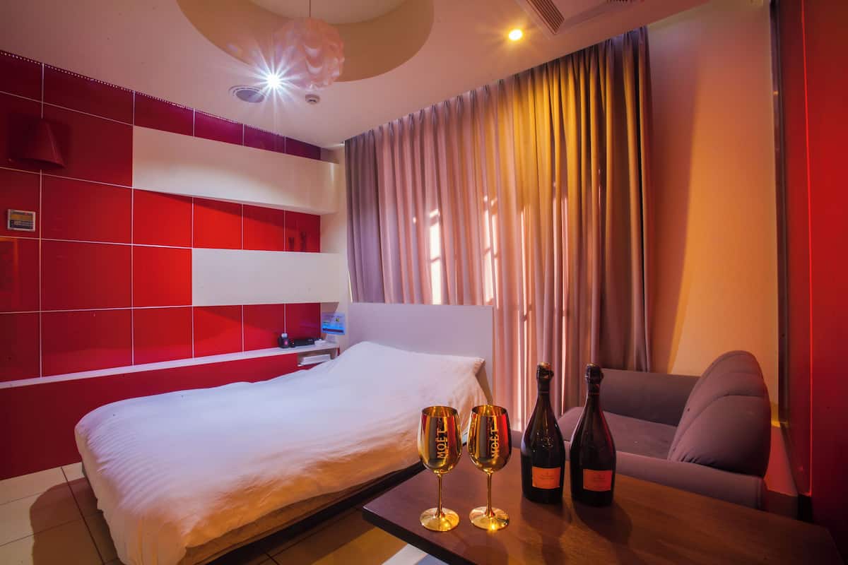 A hotel room with a bed, a table with two champagne glasses and a bottle, a sofa, and a curtain.