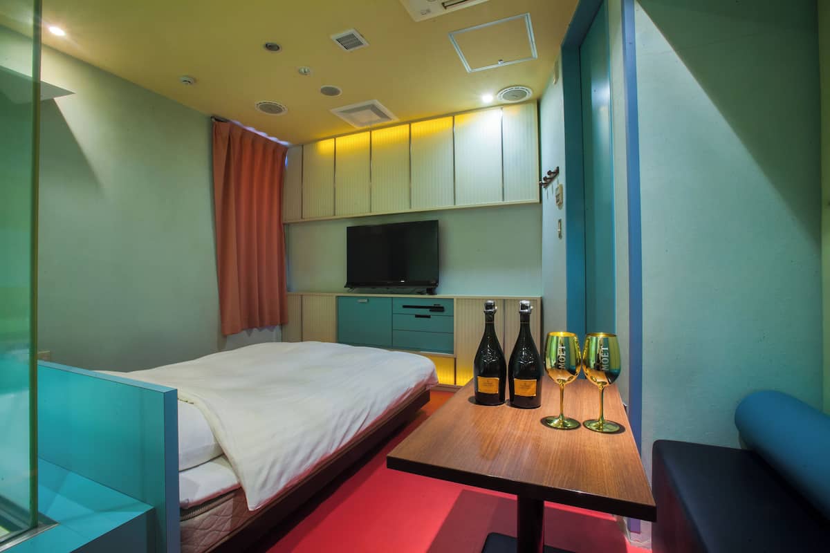 A hotel room with a bed, a TV, a table with wine bottles and glasses, and a small kitchenette.