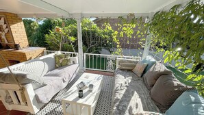 Een overdekt terras met een witte bank, een klein tafeltje en een vloer met een patroon.