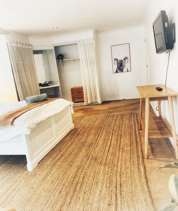 A bedroom with a bed, a wooden desk, a television, and a mirror.