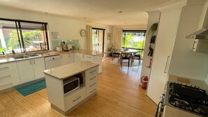 Een moderne keuken met witte kastjes, een centraal eiland, een eetgedeelte met een ronde tafel, en uitzicht op groen buiten.