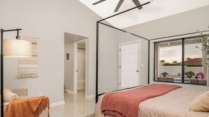 A bedroom with a large bed, a bedside table, a mirror, and a view of the outdoors.