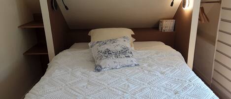 A bedroom with a bed, two pillows, a nightstand, and a wall-mounted lamp.