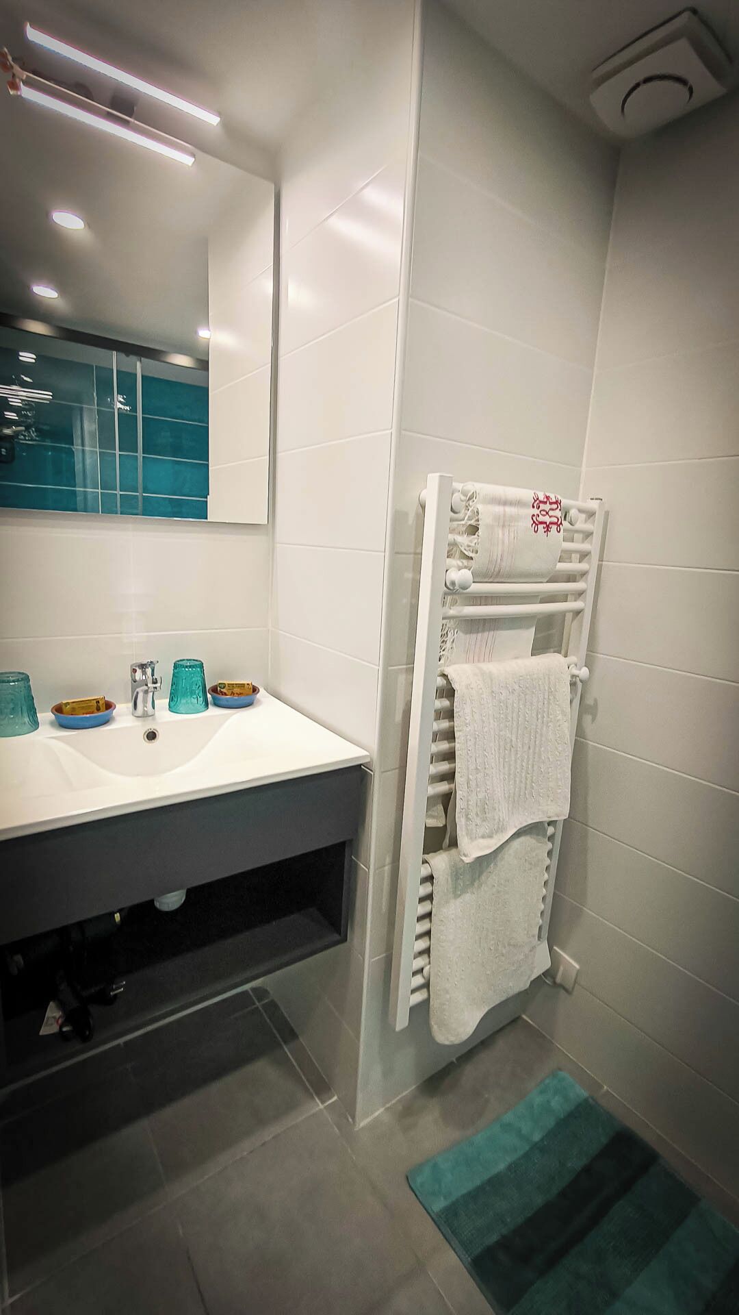 Un baño moderno con un lavamanos, espejo y toallero blancos.