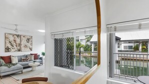 Una sala de estar moderna con un sofá gris, una mesa de centro y una escalera que lleva a un balcón con vista a la piscina.