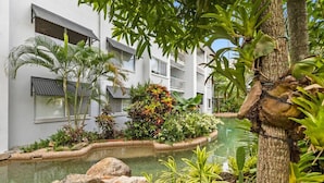 Una piscina rodeada de plantas tropicales y un edificio blanco con balcones.