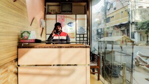 A reception area with a counter, a person standing behind it, and a view of the street outside. - Hotel Sunrise Lucknow  (Lucknow)