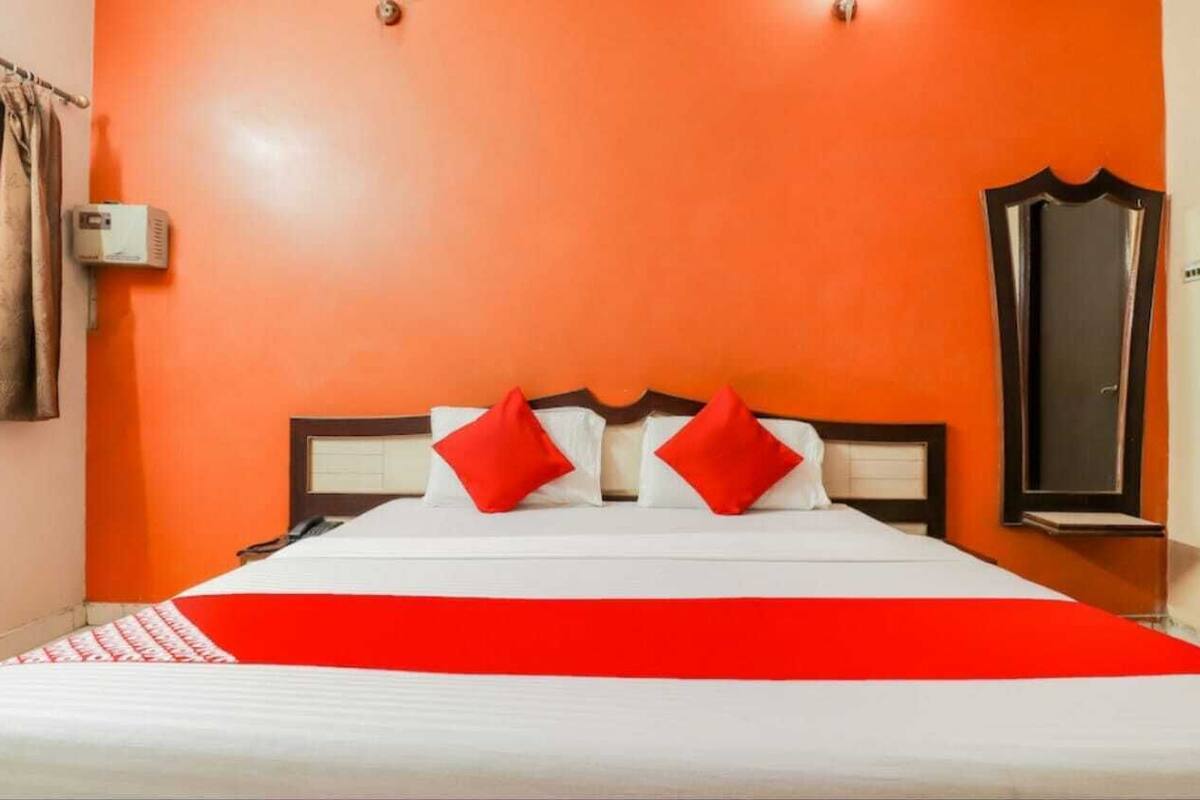 A hotel room with a bed, red pillows, and a red blanket.