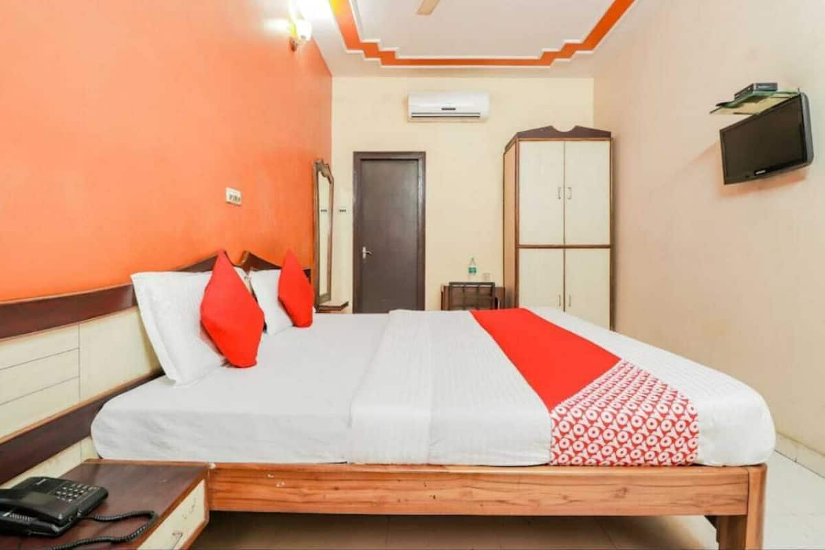 A hotel room with a wooden bed, a telephone, an air conditioning unit, a wardrobe, and a television.