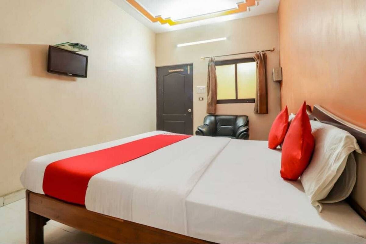 A hotel room with a bed, a television, a chair, and a window with curtains.