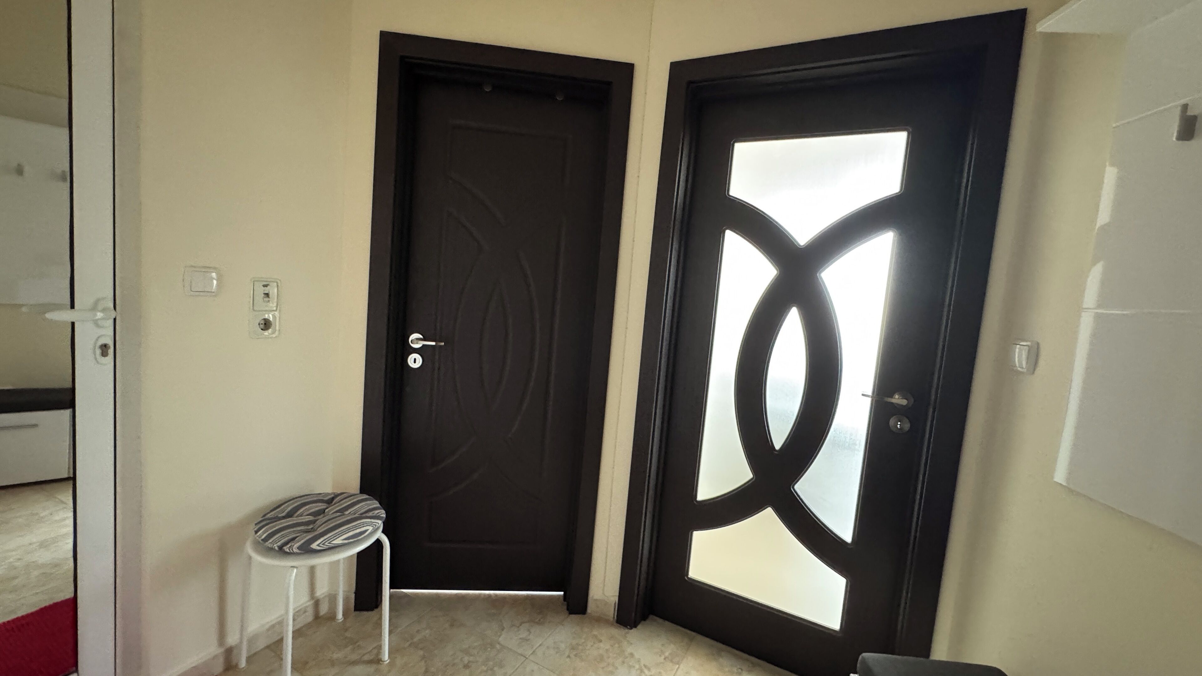 Um quarto com uma porta escura, um pequeno banquinho e um interruptor de luz na parede.