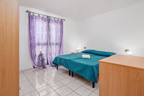 Une chambre à coucher avec un lit, une commode en bois, une table de chevet et une fenêtre ornée de rideaux violets.