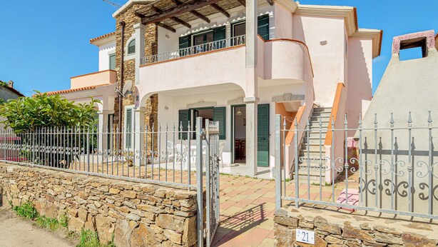 Una casa de dos pisos con un balcón, un muro de piedra y una reja de metal.
