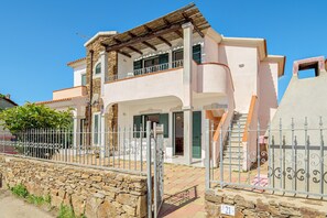 A two-story house with a balcony, a stone wall, and a metal gate.