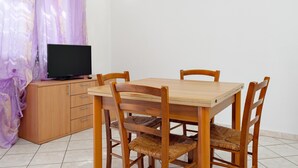 Un comedor con una mesa y sillas de madera, un televisor sobre un mueble bajo y una lámpara en la pared.