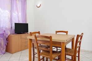 Un comedor con una mesa y sillas de madera, un televisor sobre un mueble bajo y una lámpara en la pared.