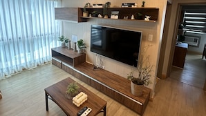 A modern living room with a large flat-screen TV, wooden flooring, a coffee table, and built-in shelves with decorative items.