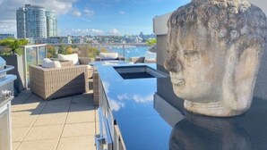 A rooftop terrace with a stone sculpture, outdoor furniture, and a view of the city skyline.