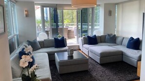 A modern living room with grey sofas, a coffee table, and a large window offering a view of the outdoors.