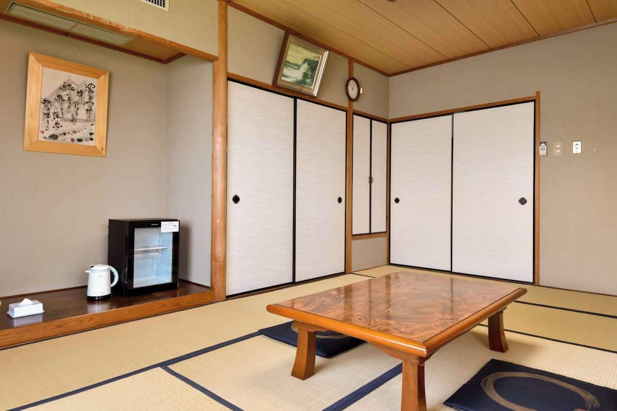 A traditional Japanese room with tatami flooring, a wooden table, a refrigerator, a telephone, and a clock on the wall.