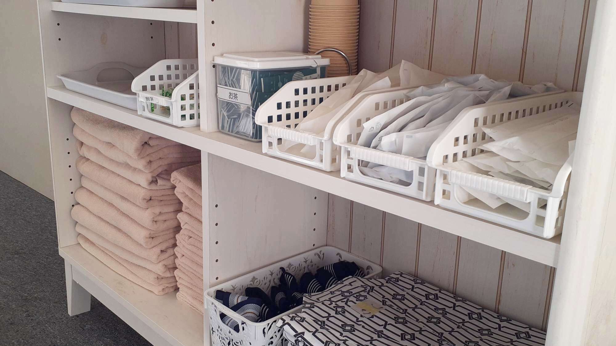 A storage unit with shelves holding folded towels, plastic baskets, and a basket with patterned items.
