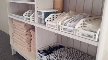 A storage unit with shelves holding folded towels, plastic baskets, and a basket with patterned items.