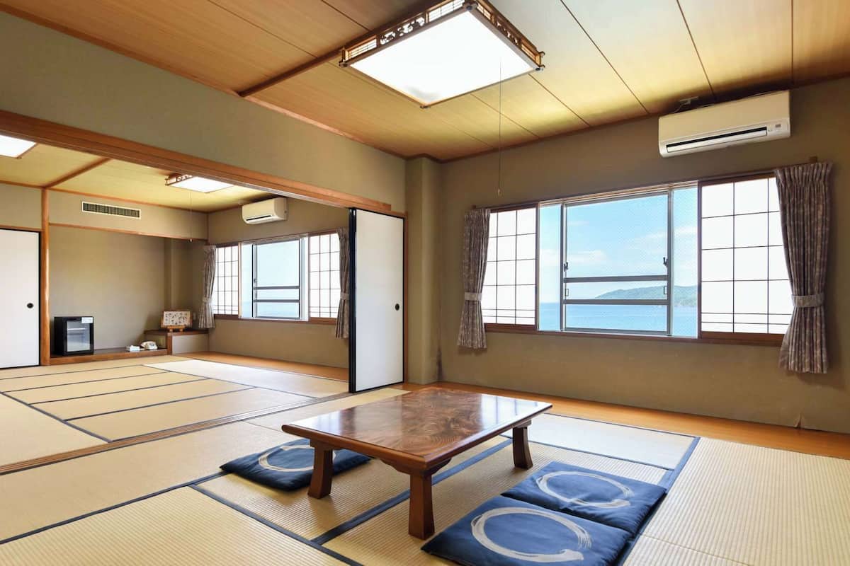 A traditional Japanese room with tatami flooring, a sliding door, a table, and a view of the sea.