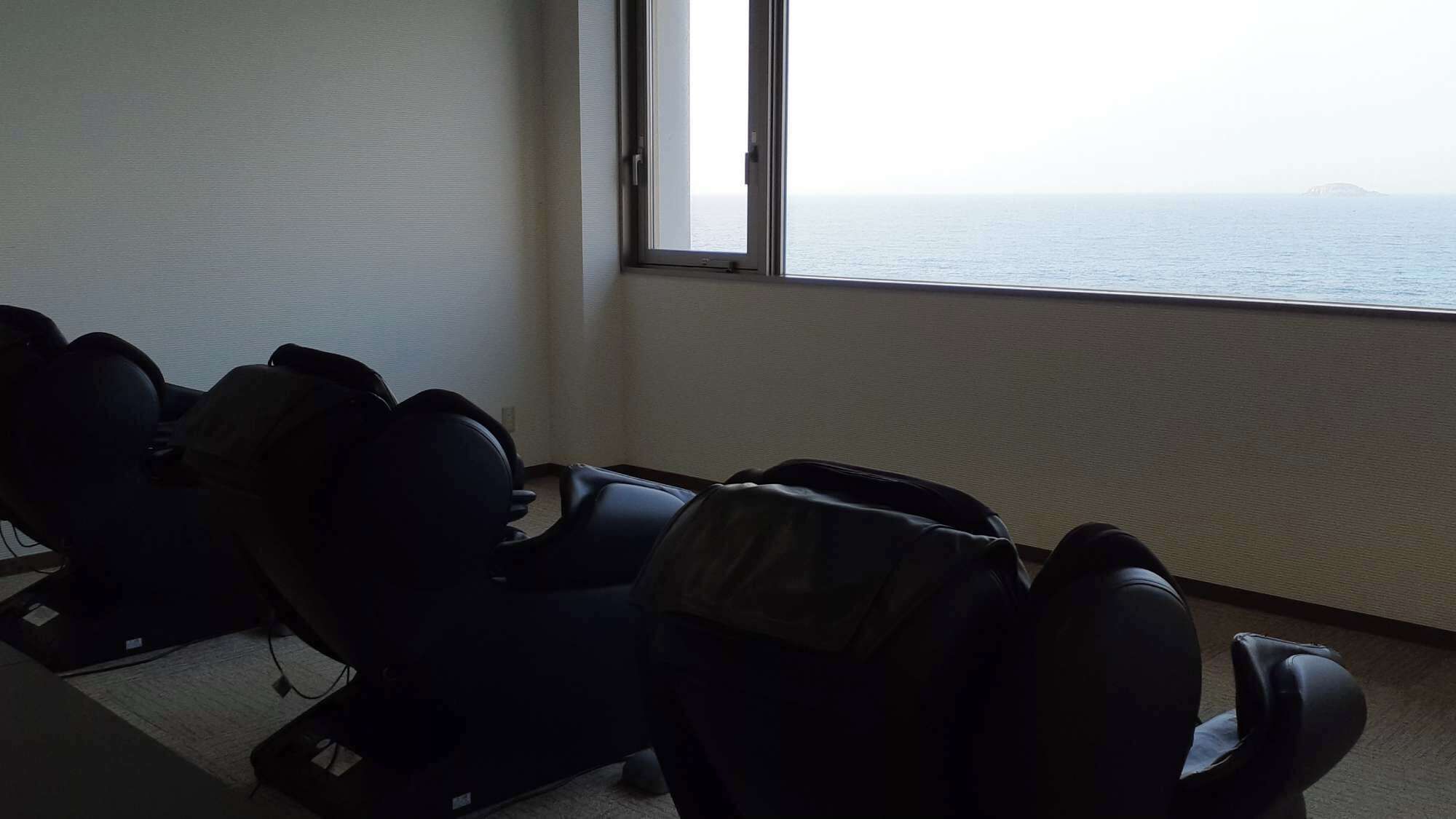 A room with massage chairs and a large window overlooking the sea.