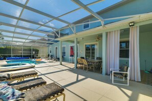 A covered outdoor area with a pool, lounge chairs, and a table with chairs.