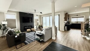 A spacious living area with a fireplace, a sofa, and a coffee table. There is a kitchen area with a sink and cabinets.