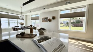 A modern kitchen with a large island, a dining area with chairs, and large windows offering a view of the outdoors.