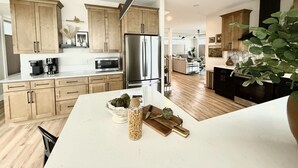 A modern kitchen with wooden cabinets, stainless steel appliances, and a central island with a bowl of artichokes and a knife block.