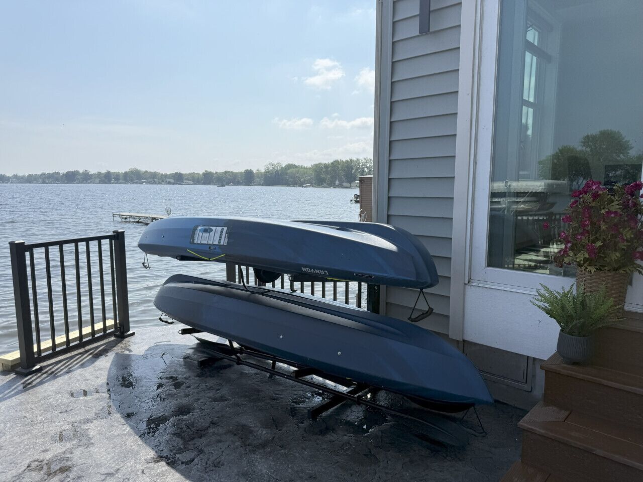 Two kayaks on a concrete surface near a house with a view of a lake.