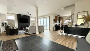 A spacious living room with a fireplace, grey sofas, a black coffee table, and a black rug. - Huge 6BR Oneida Lakefront Retreat - Sleeps 20! (Cicero)