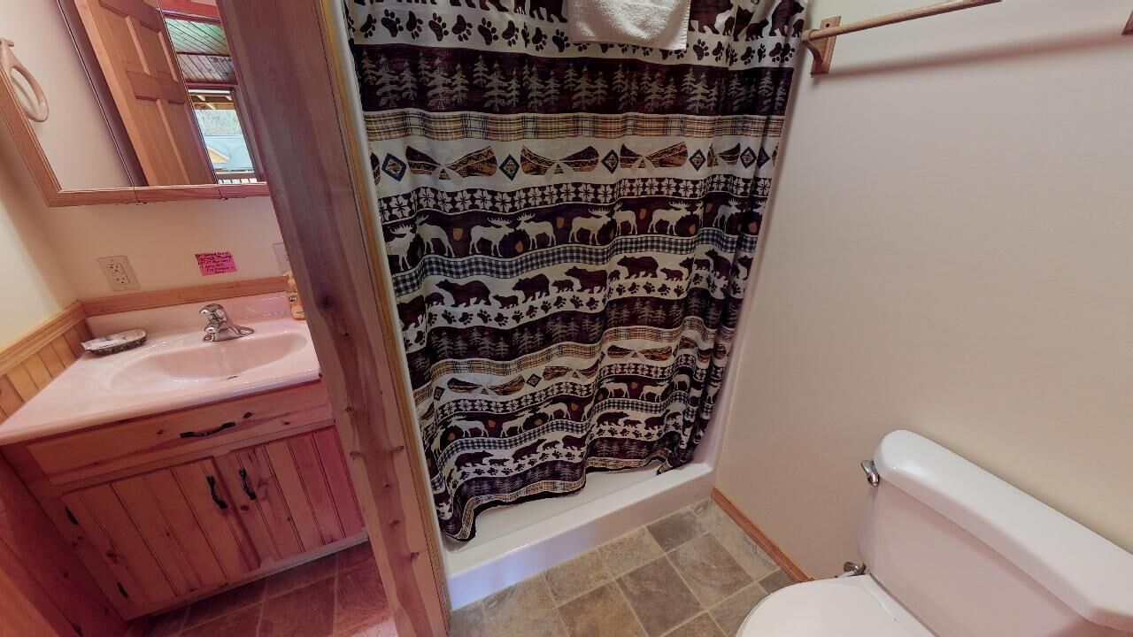 A bathroom with a wooden vanity, a sink, a toilet, and a shower curtain with a patterned design.