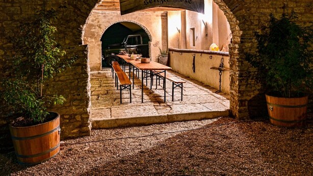 Un área de comedor al aire libre con muros de piedra, mesas de madera, bancos y plantas en macetas.