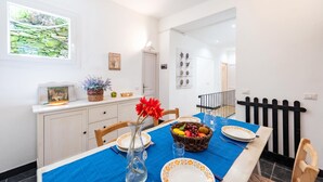 A dining area with a table set for two, a window with a view of greenery, and a door leading to another room. - Charming Apartment With Balcony In Vernazza (Vernazza)