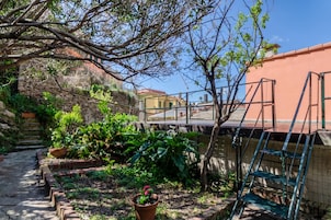 Um jardim com diversas plantas, um muro de pedra e uma escadaria de metal.