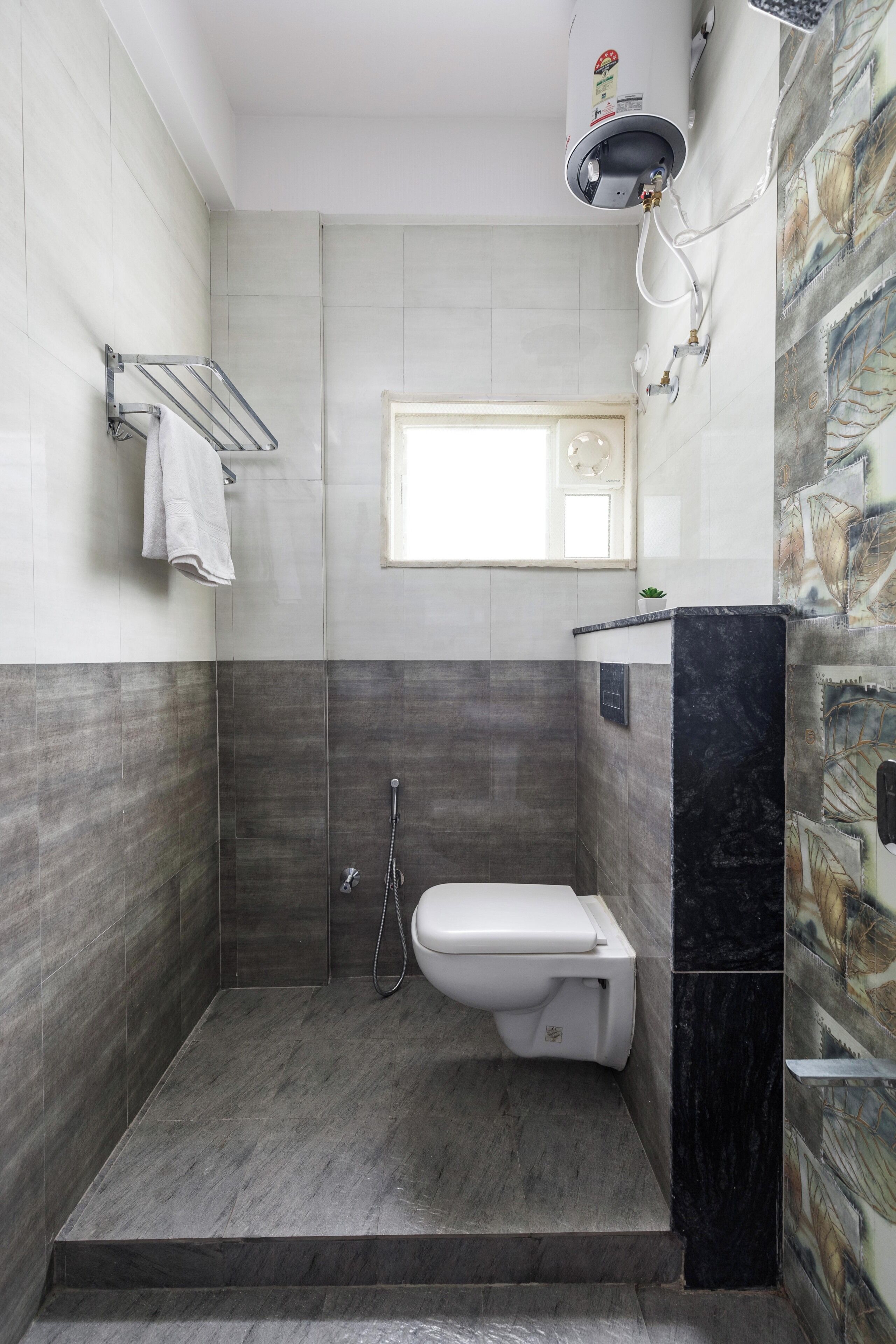 Et moderne badeværelse med bruser, toilet og håndklædestang.