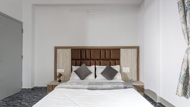 A neatly made bed with a wooden headboard, two bedside tables with lamps, and a vase with flowers on one table. - Galaxy 4th Block by Red Olive (Bengaluru)
