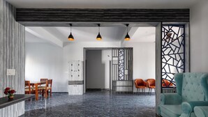 A modern living room with a marble floor, a teal sofa, and a dining area with wooden chairs and a table. - Galaxy 4th Block by Red Olive (Bengaluru)