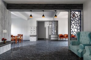 Een moderne woonkamer met een marmeren vloer, een smaragdgroene bank en een eethoek met houten stoelen en een tafel.