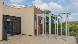 A rooftop terrace with a tiled floor, a black gate, and a white pergola structure. - Galaxy 4th Block by Red Olive (Bengaluru)
