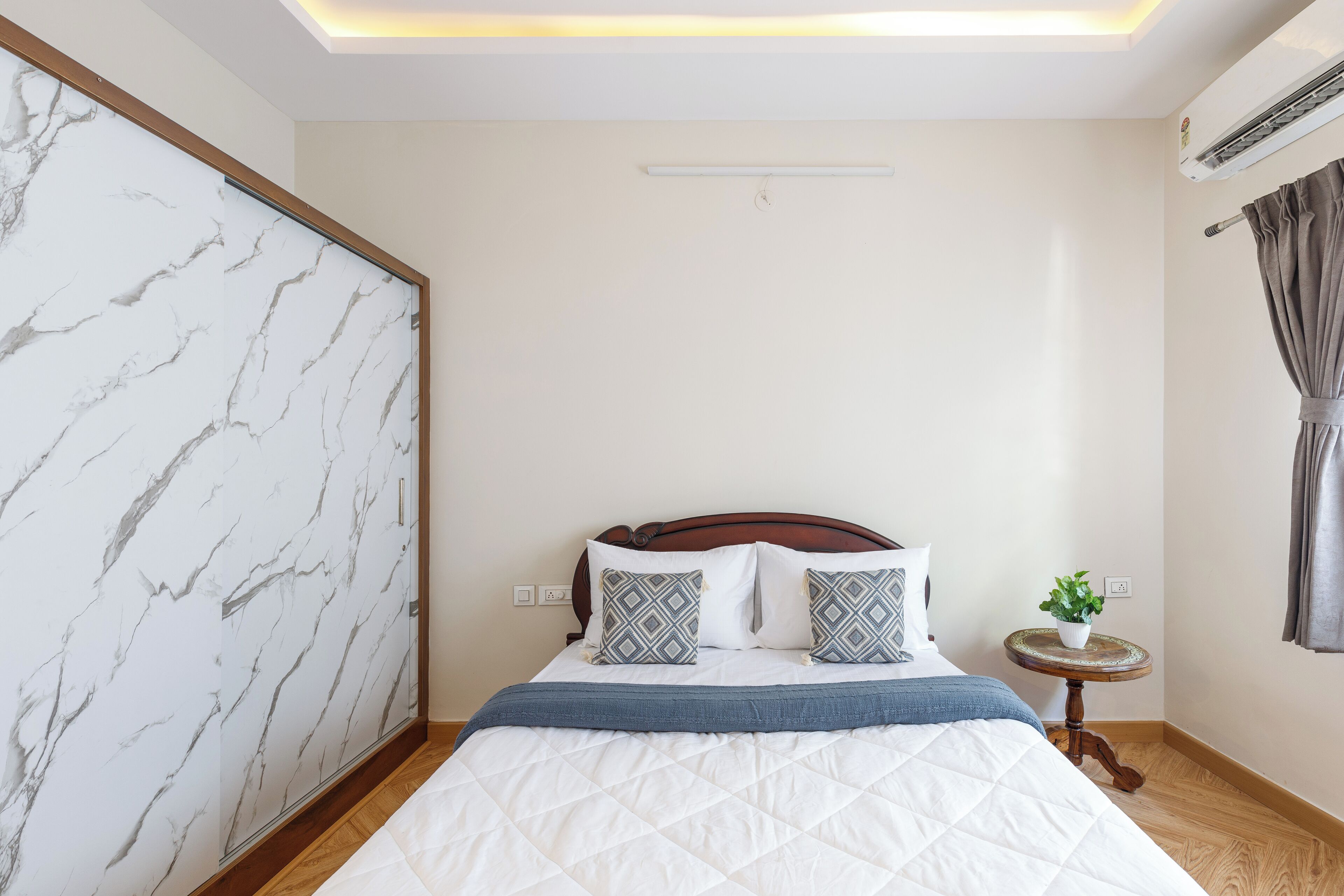 A bedroom with a bed, a nightstand, a wall-mounted air conditioner, and a ceiling light fixture.
