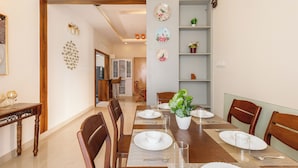 Un coin repas avec une table en bois, dressée pour quatre personnes, entourée de chaises. Un pot de fleurs est posé sur la table, et des assiettes décoratives ornent le mur.
