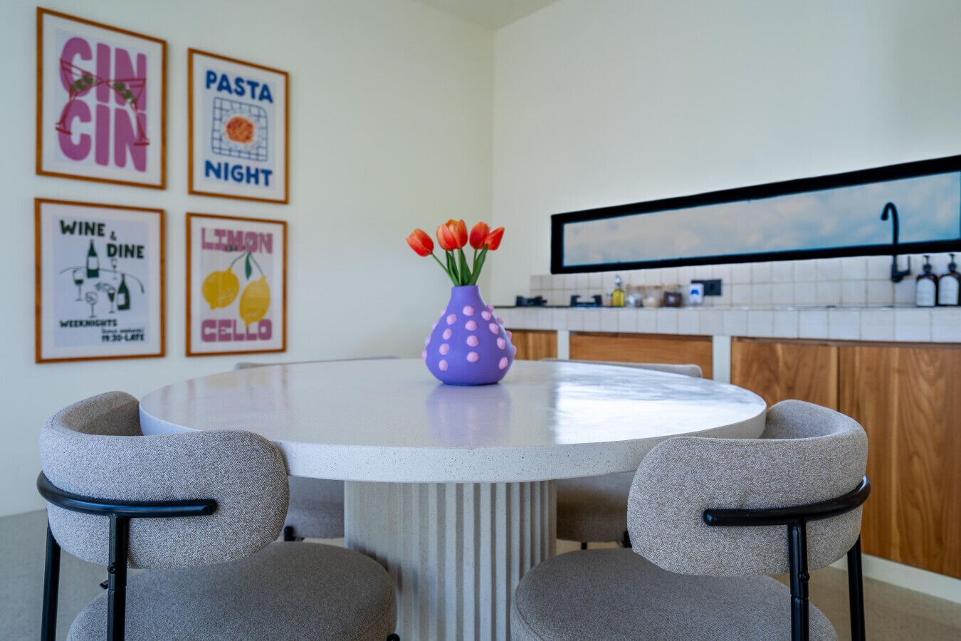 A modern kitchen with a round dining table, two grey chairs, and a purple vase with red tulips.